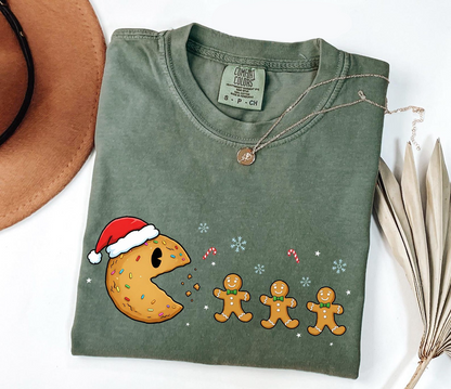 Folded green t-shirt with Christmas-themed design featuring a cookie and gingerbread men on a white surface.